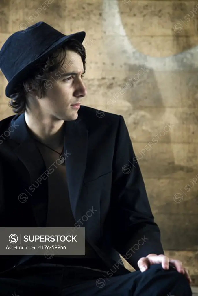 A young man looking away, wearing suit and hat