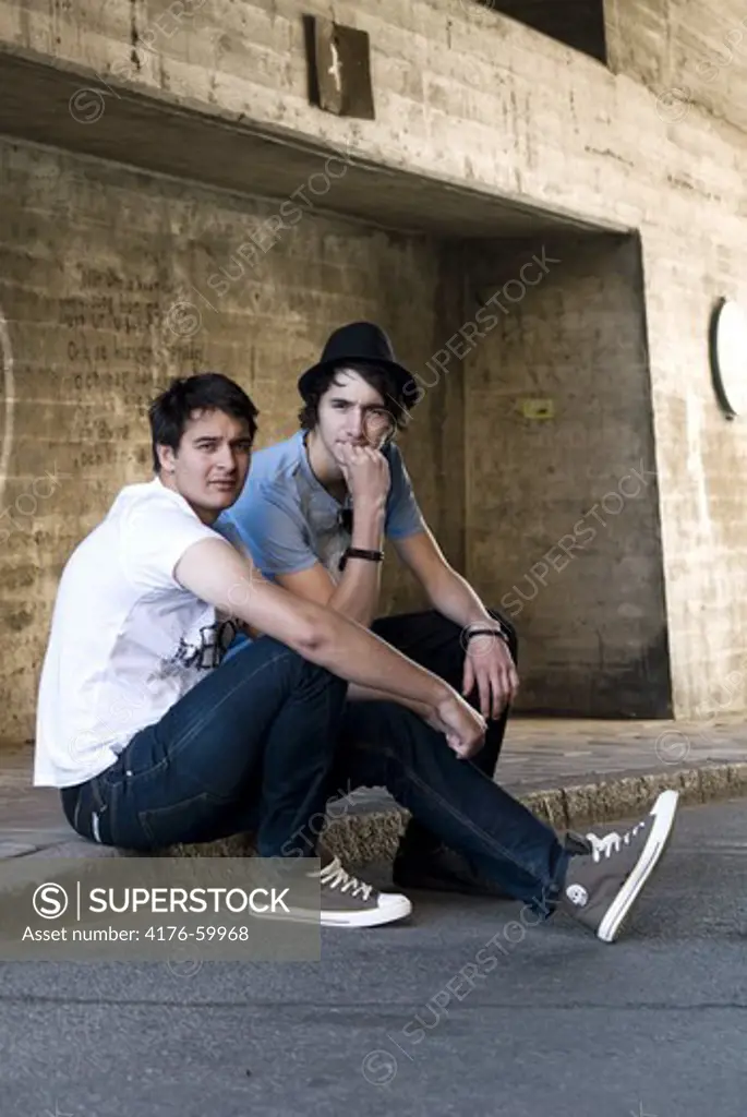 Two teenagers sitting on a sidewalk
