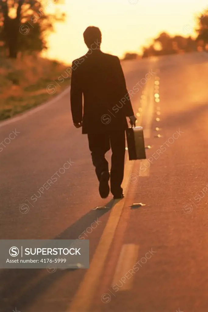 Businessman with briefcase walking endless highway at dawn