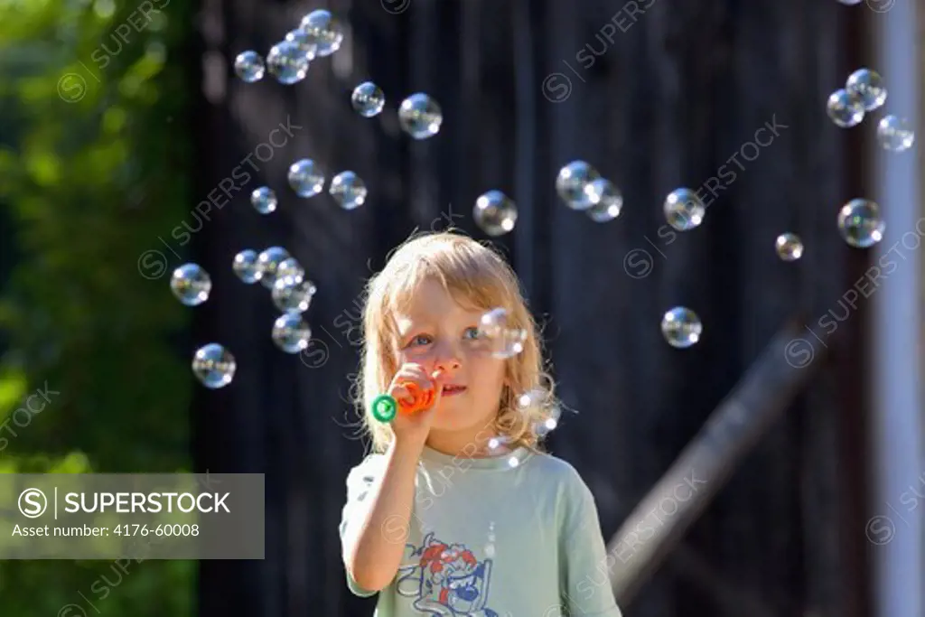 boy with long blond hair blowing sopa bubbles