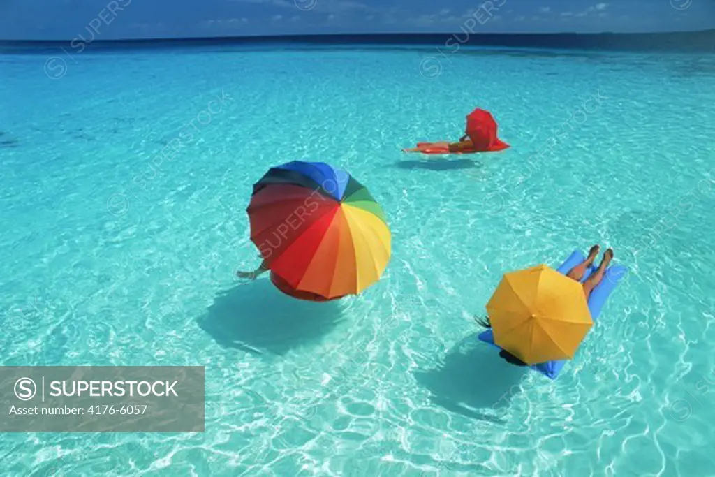 Trio of vacationers on air mattresses under colorful parasols on aqua waters
