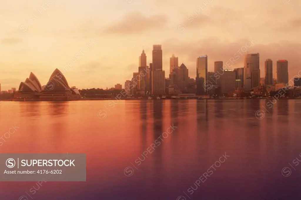 Sydney city skyline with Opera House reflecting off calm harbour waters at sunrise
