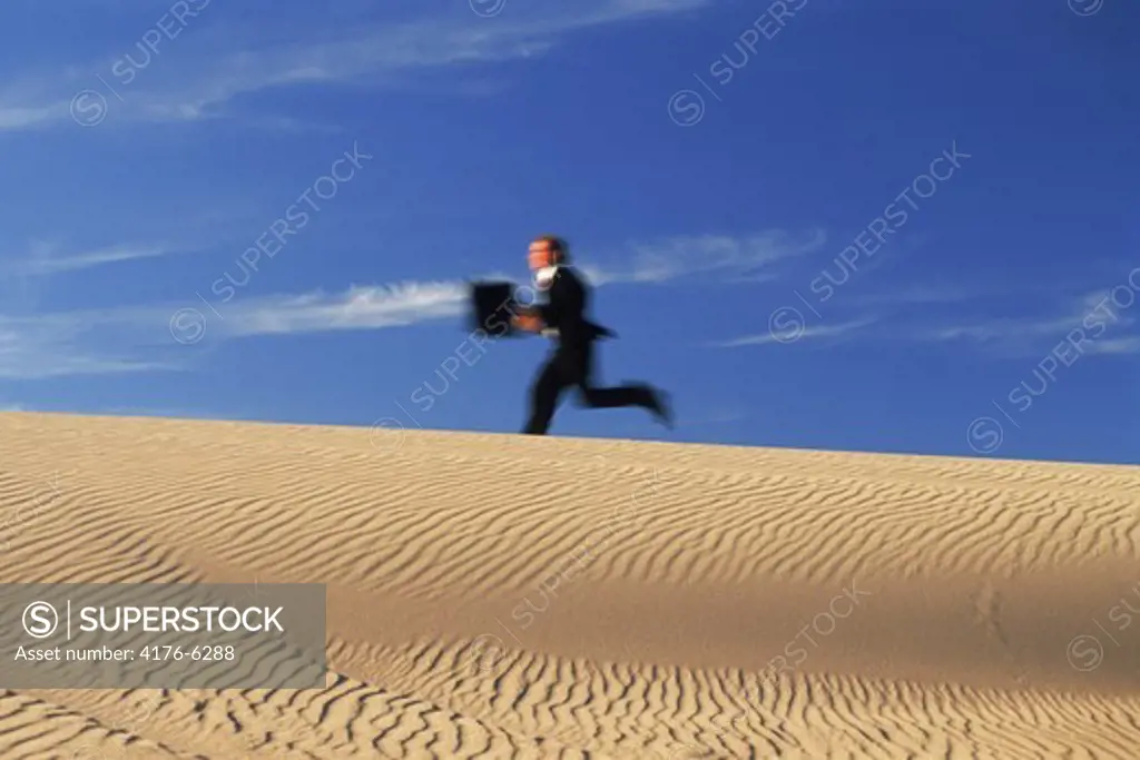 Businessman running with briefcase across sand dune