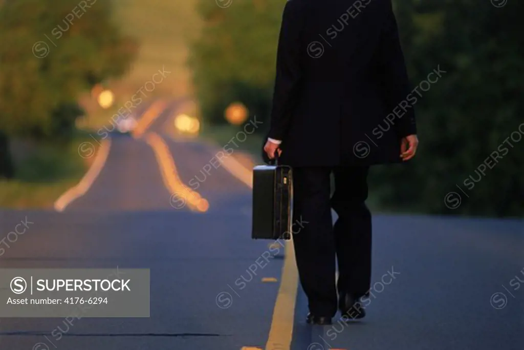 Businessman with briefcase alone on yellow lined country road