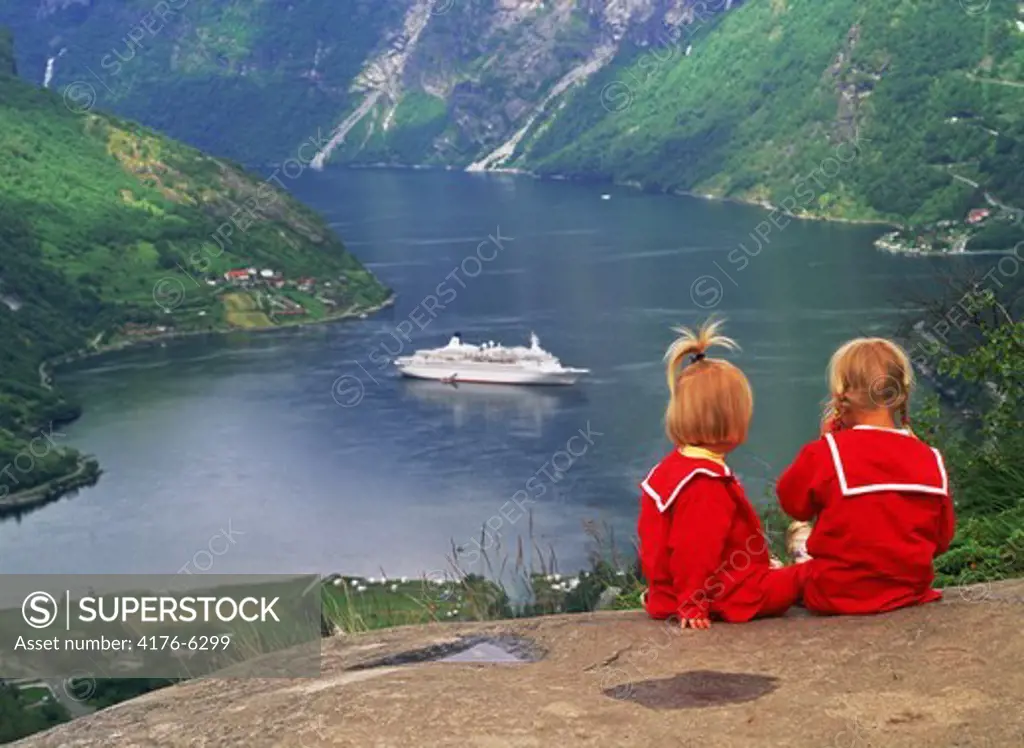 Sisters in red dresses sitting above Geirangerfjord with Norwegian passenger ship