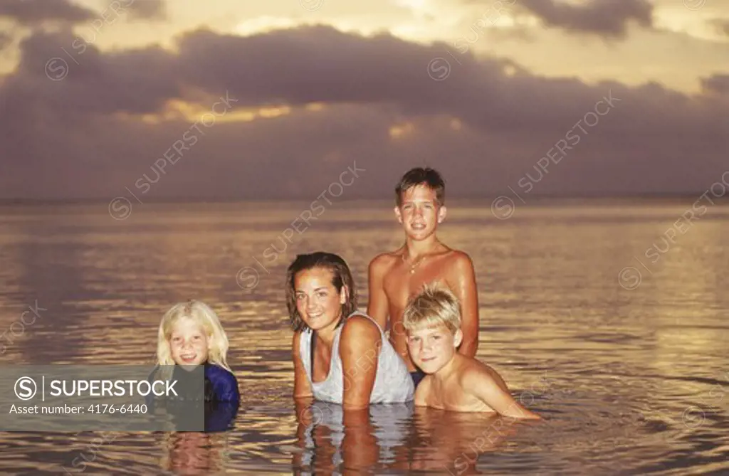 Four children in Aitutaki lagoon in South Pacific at sunset