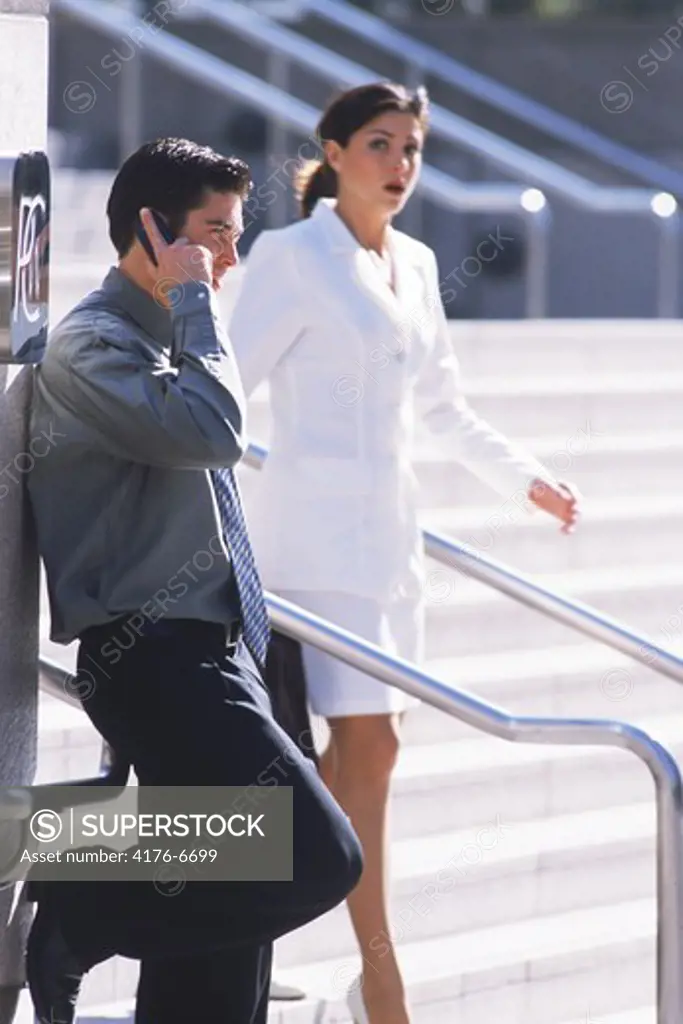 Businessman talking on cellphone with businesswoman passing