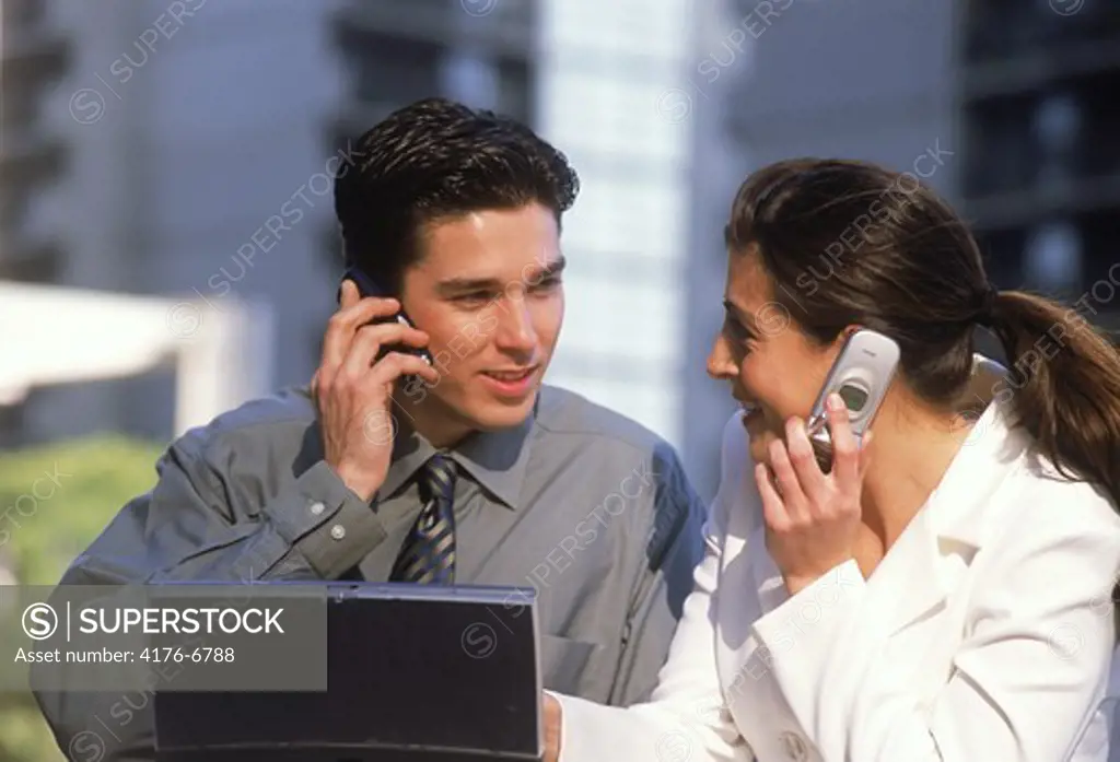 Businessman and woman with laptop and cellphones outdoors