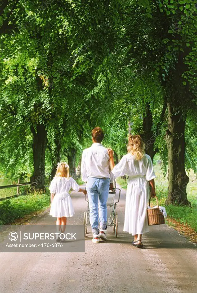 Family with baby stroller on tree lined country road in Sweden