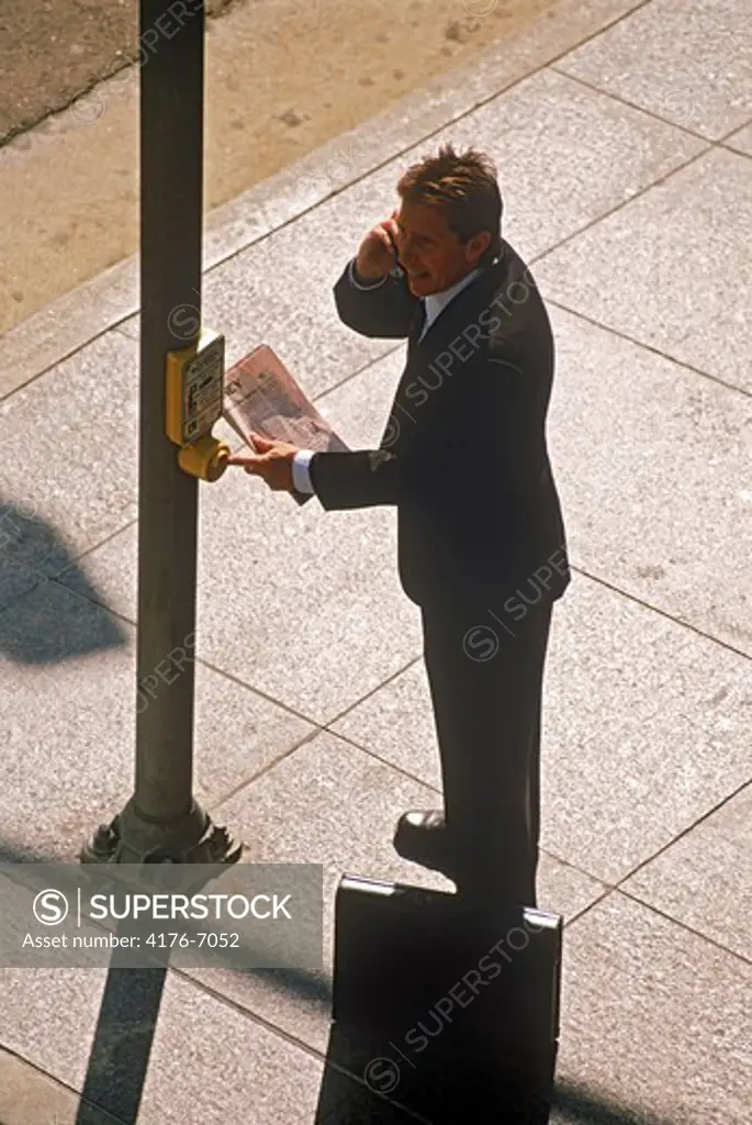 Businessman with cellphone newspaper and briefcase waiting to cross city street