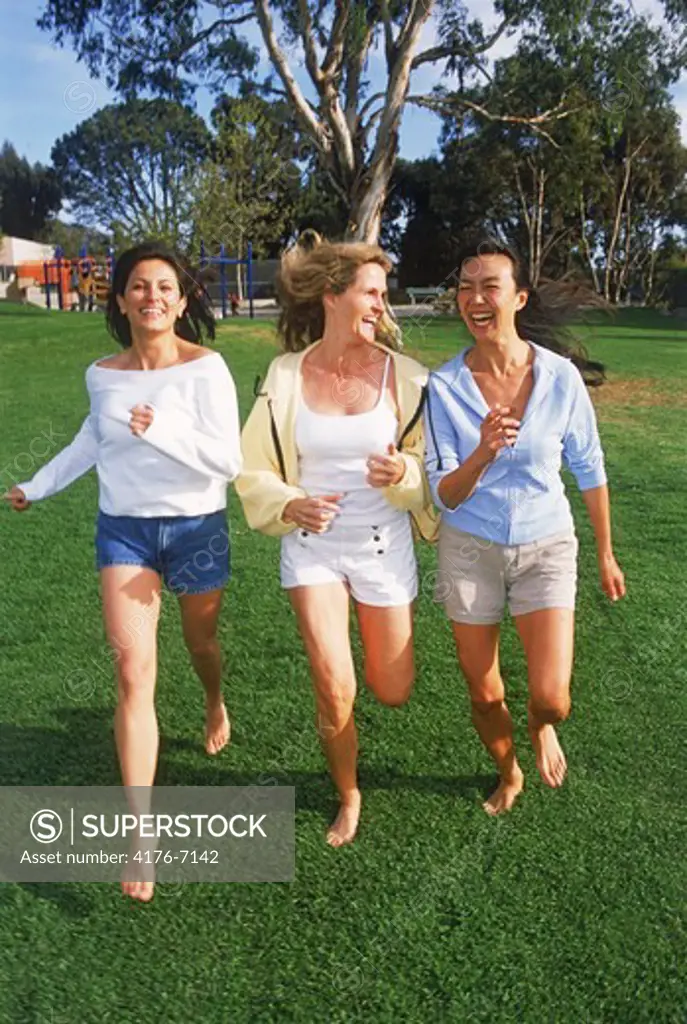 Three woman of ethnic mix running barefoot in the park