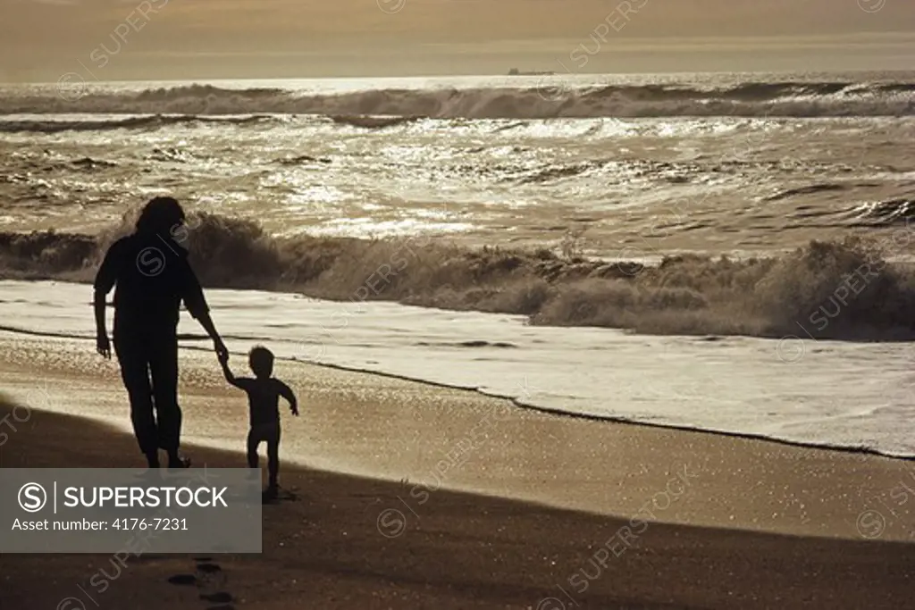 Mother and child silhouetted on wave painted open shore