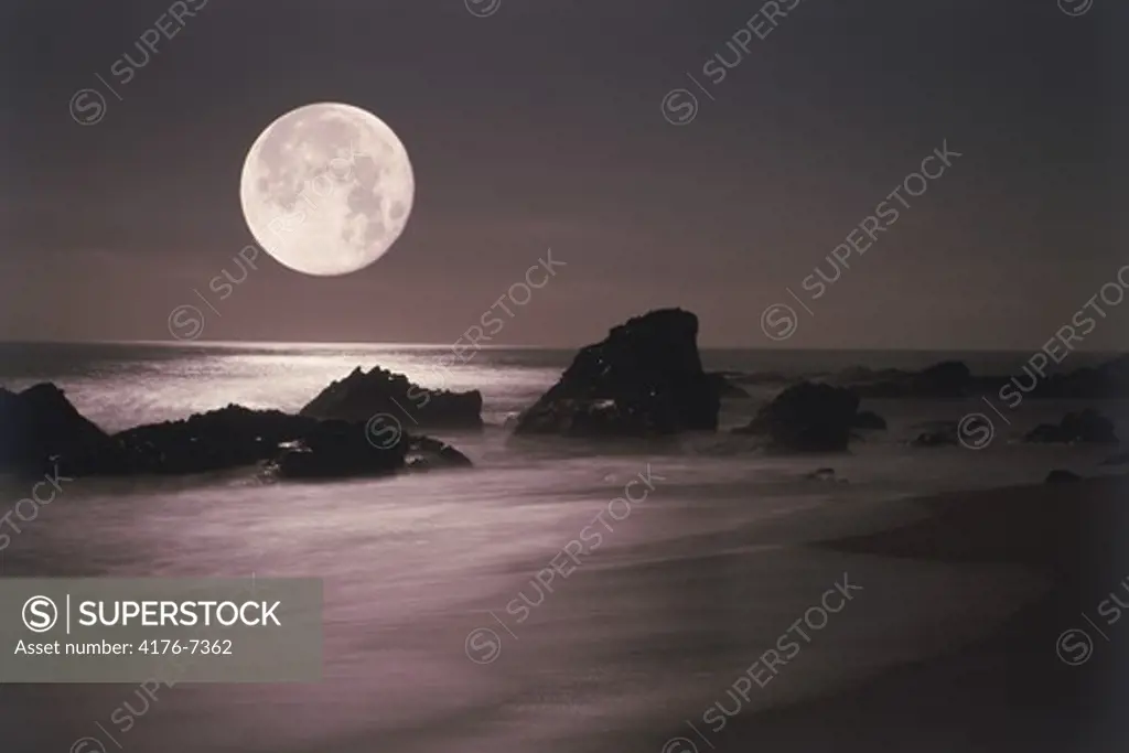 Moon setting over rocky shore