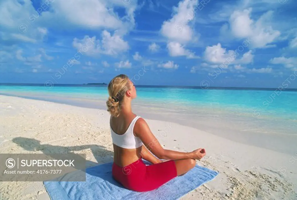 Woman on sandy shore in yoga position at dawn