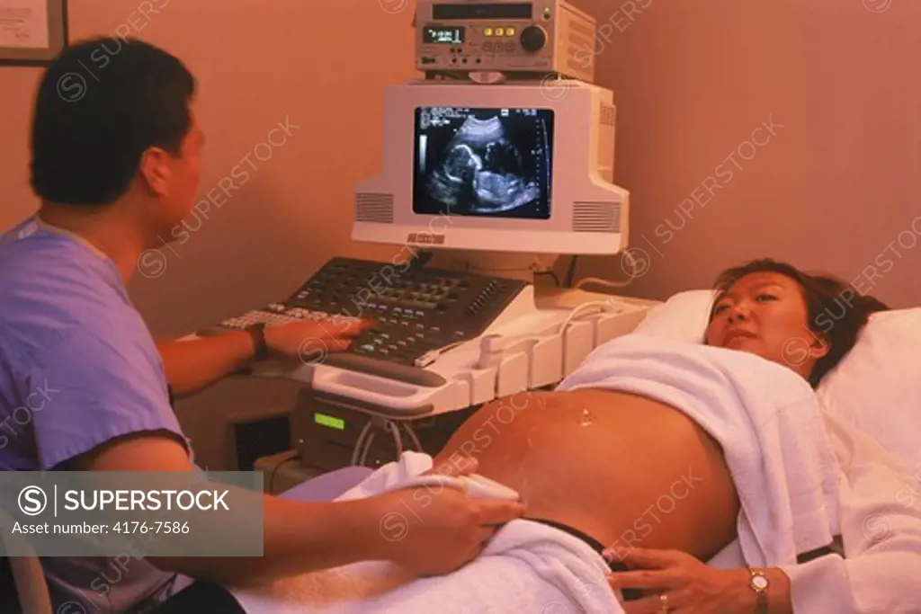 Male doctor using probe during ultrasound test with fetus on screen