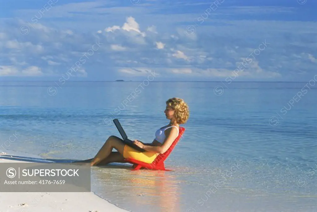 Woman on sandy shore with laptop during working holiday