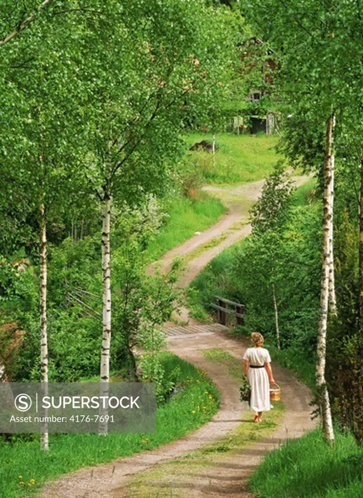 Woman with basket walking on country road in Sweden
