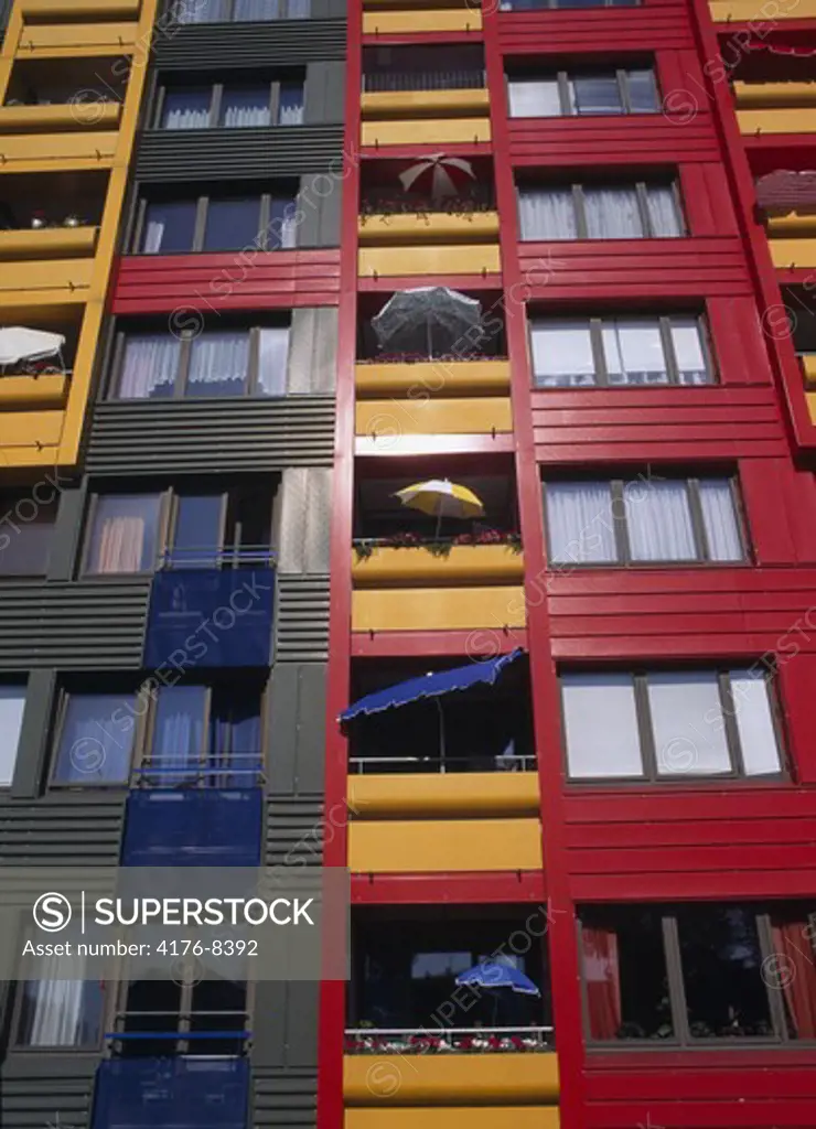Low angle view of colourful apartment building with umbrellas and glass windows