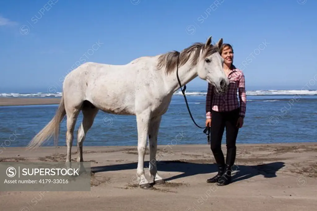 Arabian Horse and lady rider dismounted at edge of surf; Northern California, USA (Released)