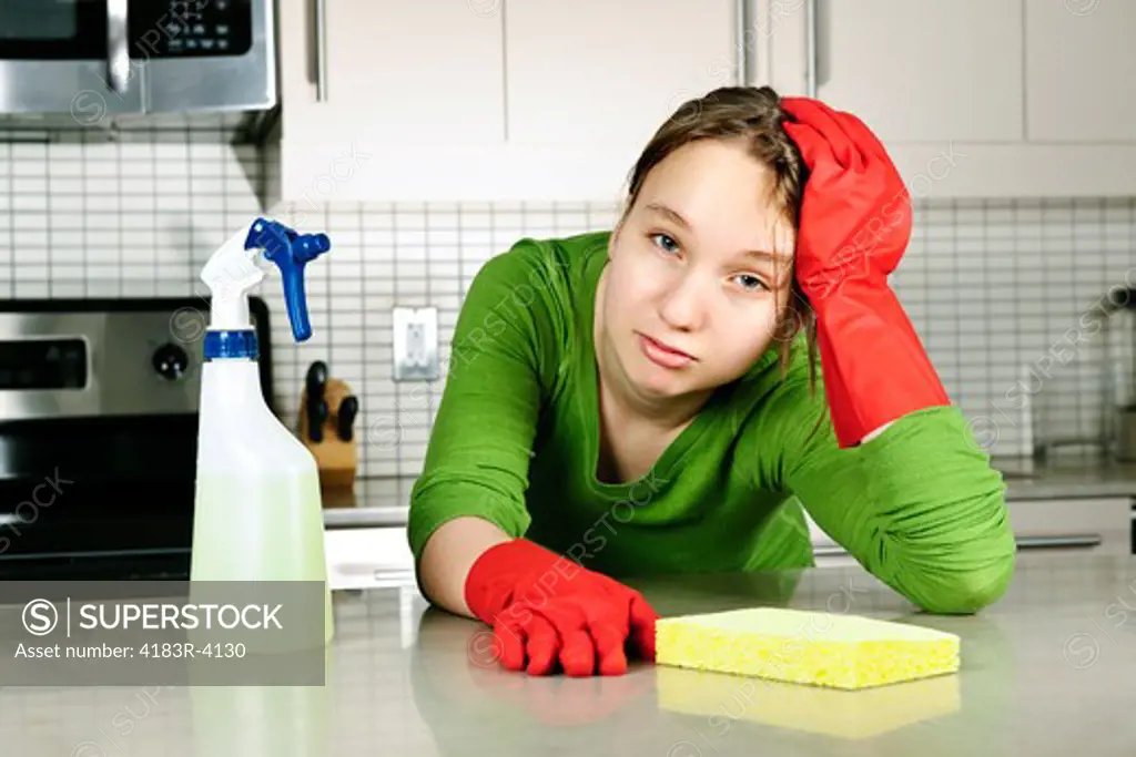 Tired girl doing kitchen cleaning chores with rubber gloves