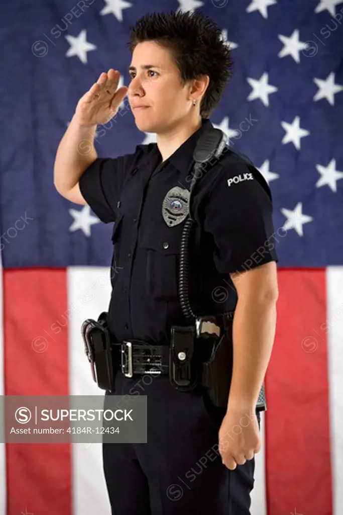Portrait of mid adult Caucasian policewoman saluting with American flag as backdrop.