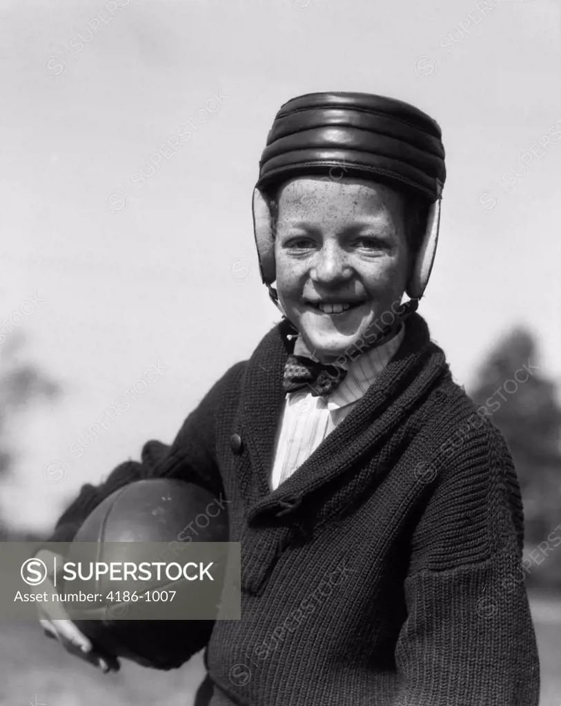 1920S Freckle-Faced Boy In Sweater & Bow Tie Wearing Leather Football Helmet Holding Football Under Arm