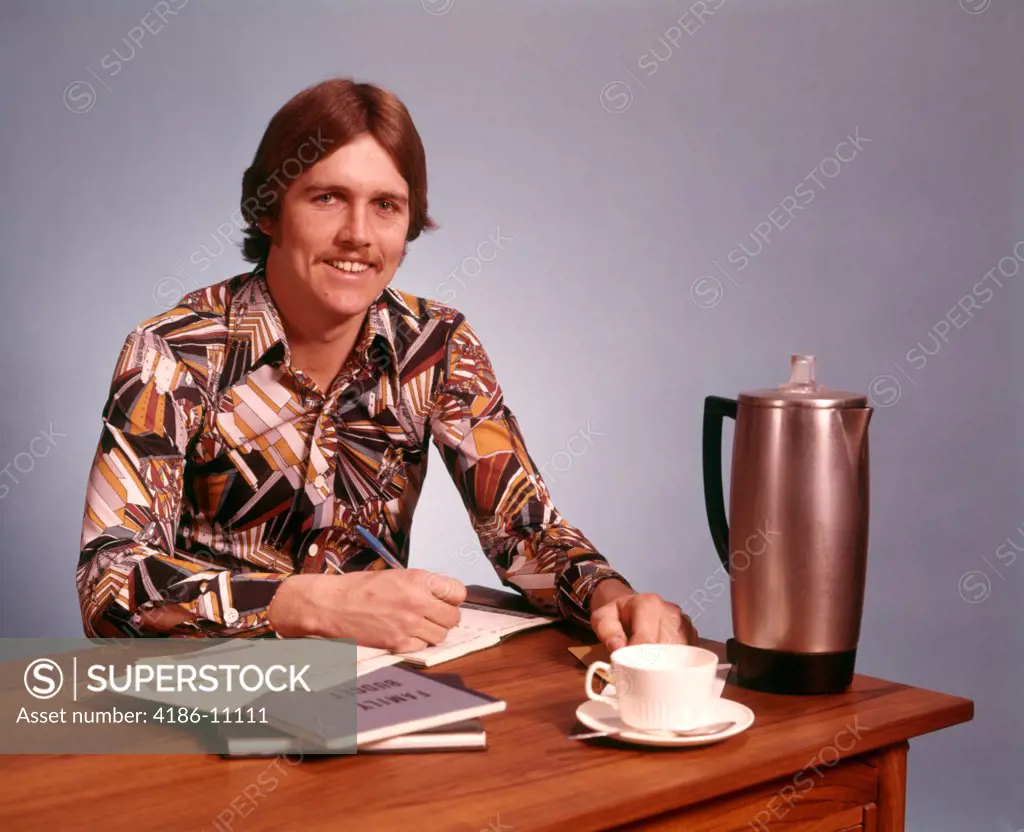 1970S Young Man Mustache Loud Print Shirt Desk Empty Coffee Cup Pot Working On Family Budget Looking At Camera 