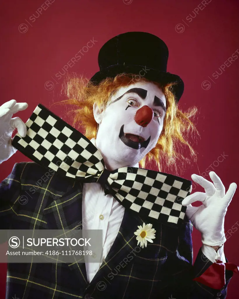 1990s CLOWN LOOKING AT CAMERA WITH HUGE CHECKERED BOW TIE A TOP HAT AND DAISY IN HIS LAPEL