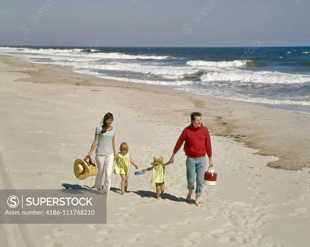 1960'S 1970'S FAMILY WALKING TOGETHER HAND HOLDING ON BEACH BY OCEAN SHORE WATER OUTDOOR MOTHER FATHER SON DAUGHTER