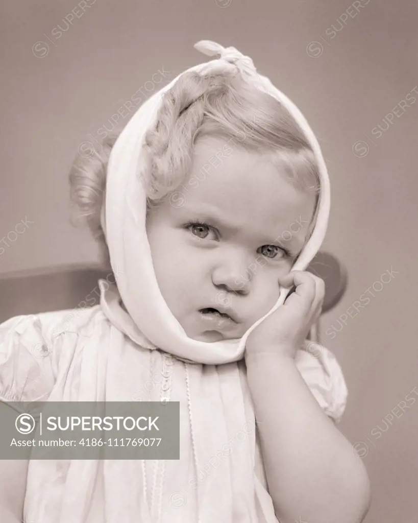1940s SICK LITTLE GIRL WITH TOOTHACHE OR MUMPS LOOKING AT CAMERA HEAD JAW WRAPPED IN COLD TOWEL TO HELP SWELLING PAIN