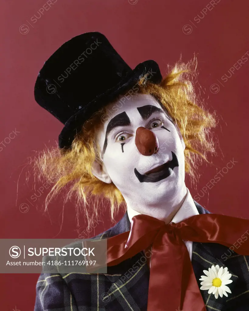 1970s SILLY WHITE FACE RED NOSE CLOWN LOOKING AT CAMERA WEARING TOP HAT ORANGE HAIR WIG PLAID JACKET AND RED RIBBON NECK TIE