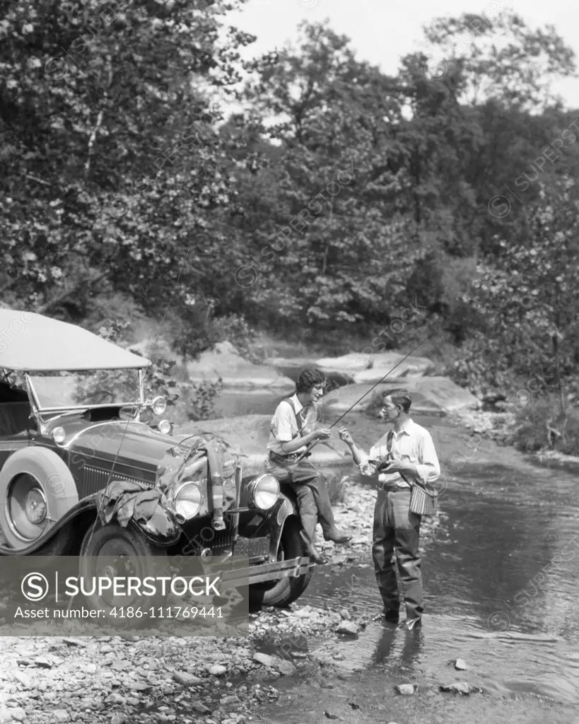 1920s COUPLE FLY FISHING MAN STANDING IN STREAM WOMAN SITTING ON