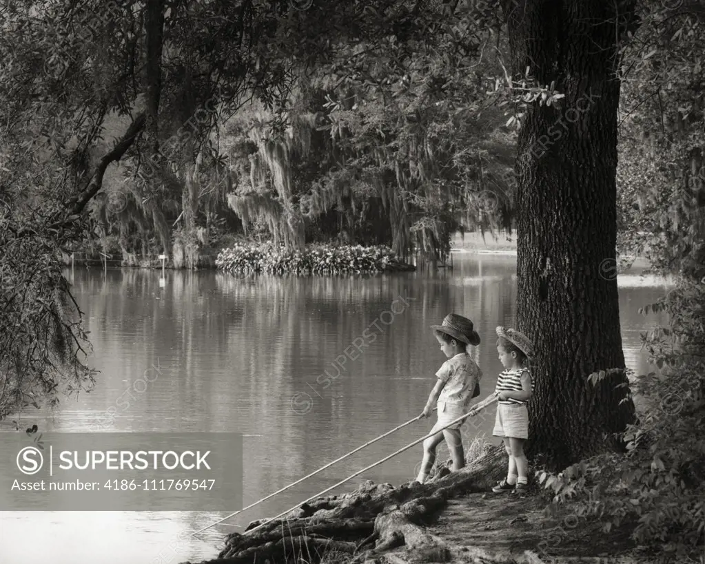 1960s LITTLE BOY AND GIRL FISHING HOLDING STICKS IN WATER BAYOU VEGETATION SPANISH MOSS HANGING FROM TREES