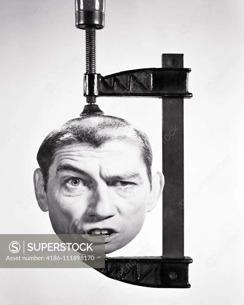 1960S 1970S MANS HEAD WITH FUNNY FACIAL EXPRESSION BEING SQUASHED IN A WOODWORKING CLAMP