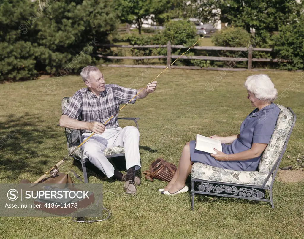 1960S Older Couple Sitting In Yard Woman Reading Man Working With Fishing Tackle Gear