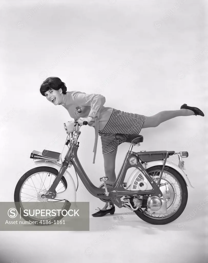 1960S 1970S Young Woman Smiling Getting On Motor Bike Or Moped With Her Leg Extended Over Back Of Bike