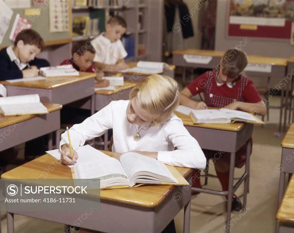 1960S Elementary School Children In Classroom At Desks Working With Books And Papers Boy Girl