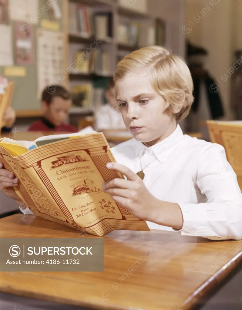 1960S Blond Girl Reading Book At Desk In Classroom