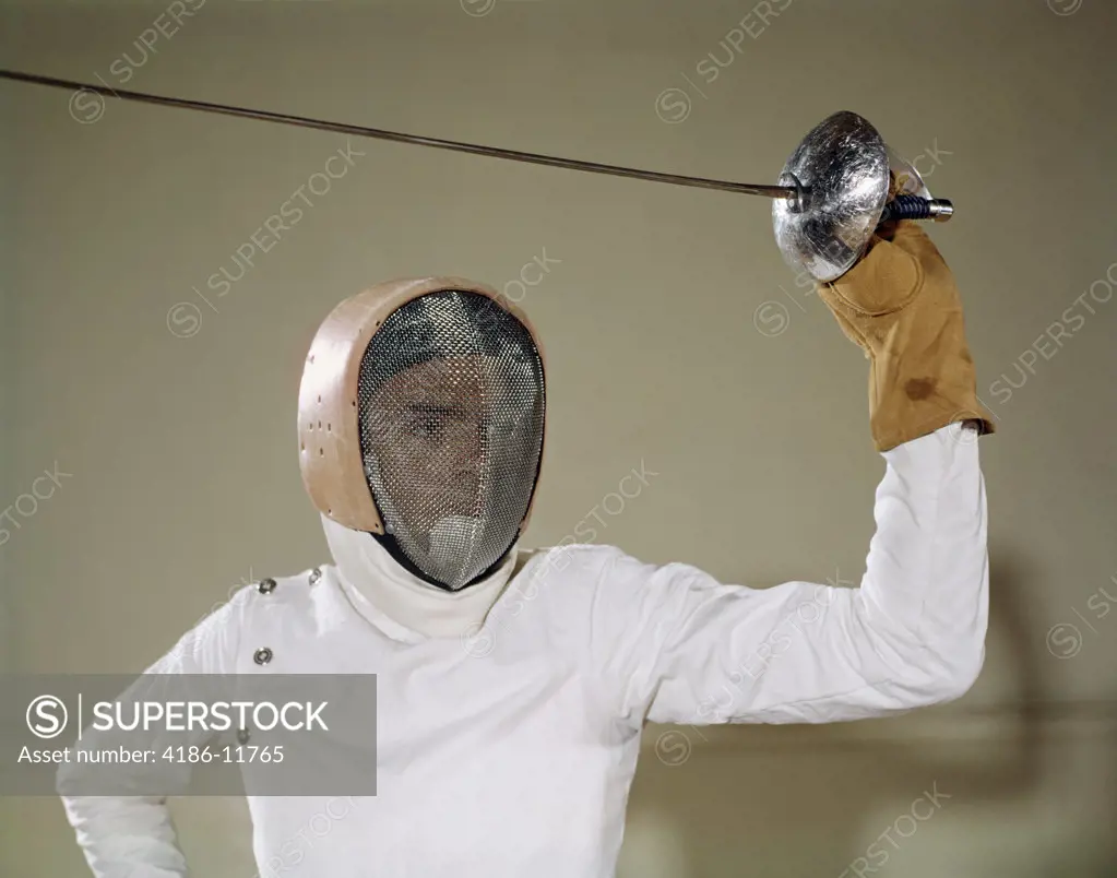 1960S Man Holding Foil Sword Epee Above His Head Wearing Helmet Protective Gear Wire Face Mask On Guard Touché Fencing