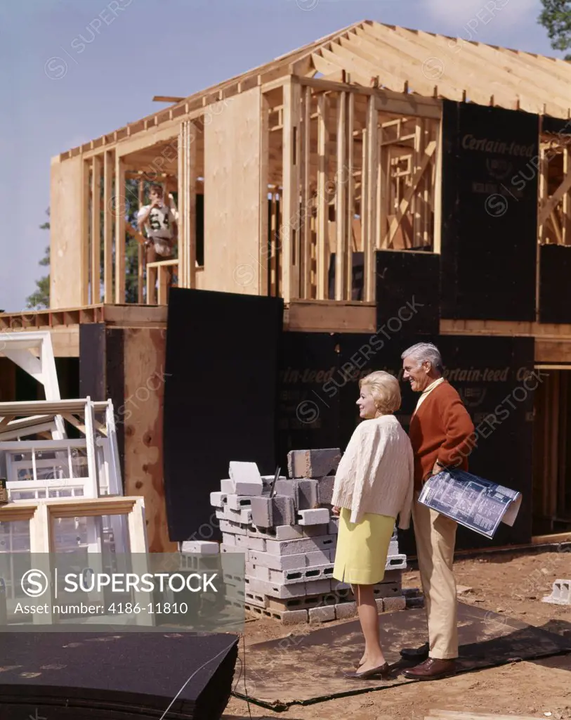 1960S Couple Looking At New Home Under Construction Building Man Woman Outdoor