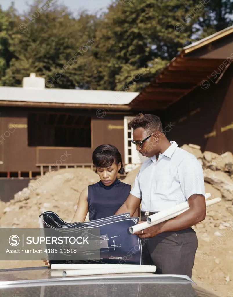 1960S African American Couple Looking At Blueprint Plans For New House Under Construction