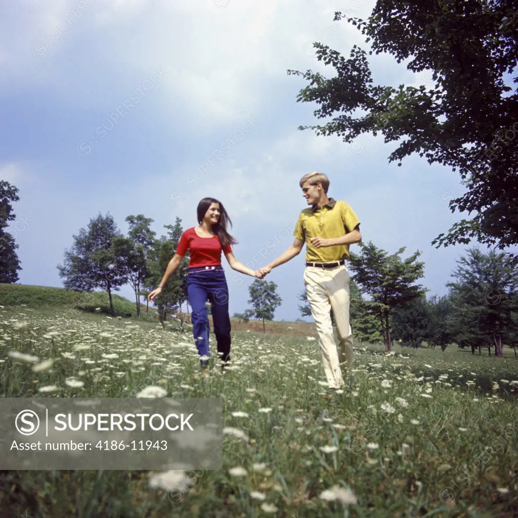 1960S 1970S Young Teen Couple Holding Hands Running Through Field Wild Flowers Queen Anne'S Lace Romance Fun Fashion