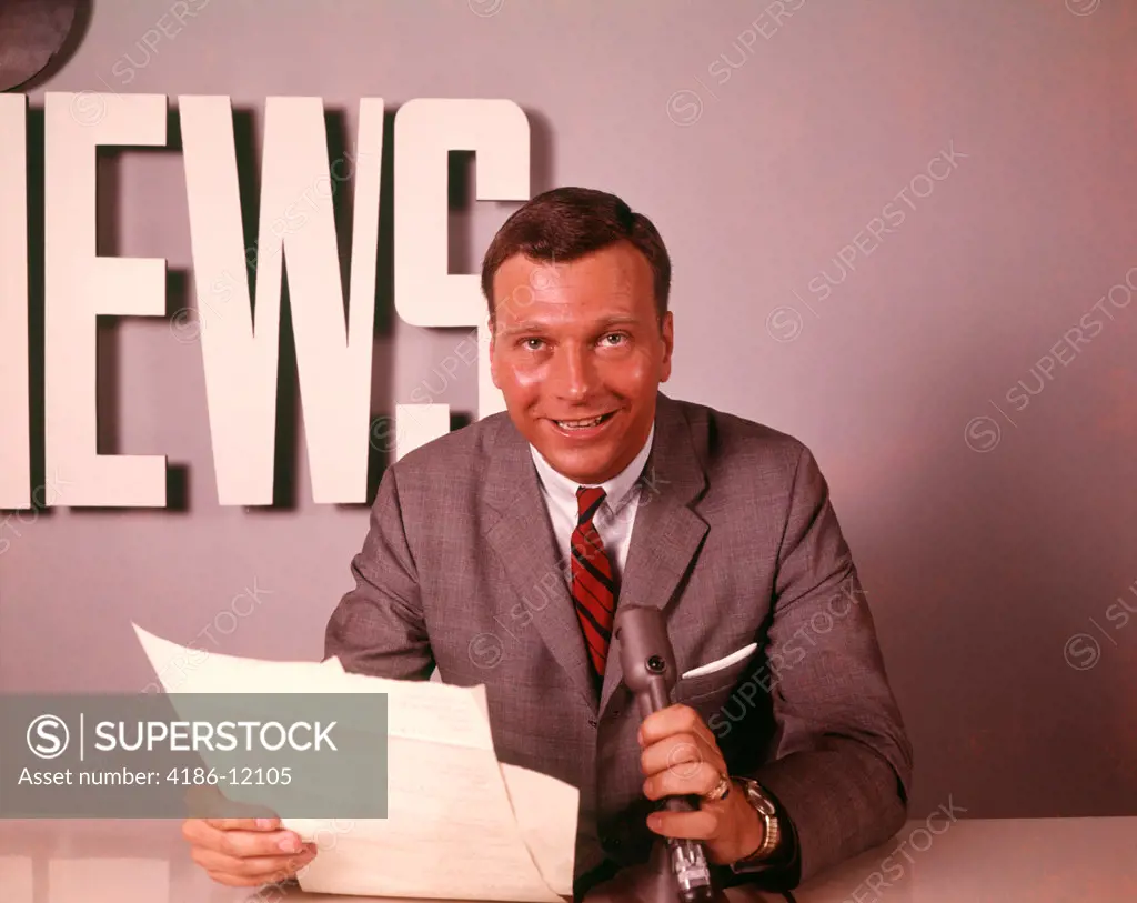 1960S Smiling Broadcast Reporter Newsman Announcer At News Desk Holding Microphone Papers Reading Report
