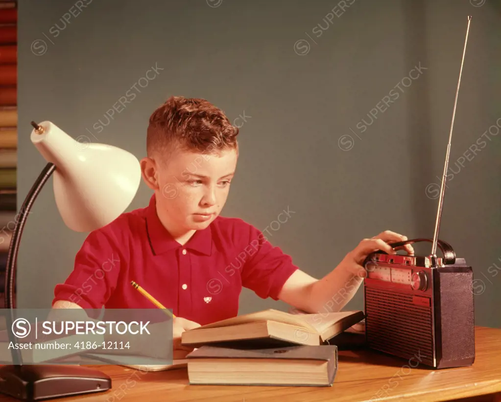 1960S Red Hair Boy Sitting At Deslistening To Portable Radio While Studying Homework  