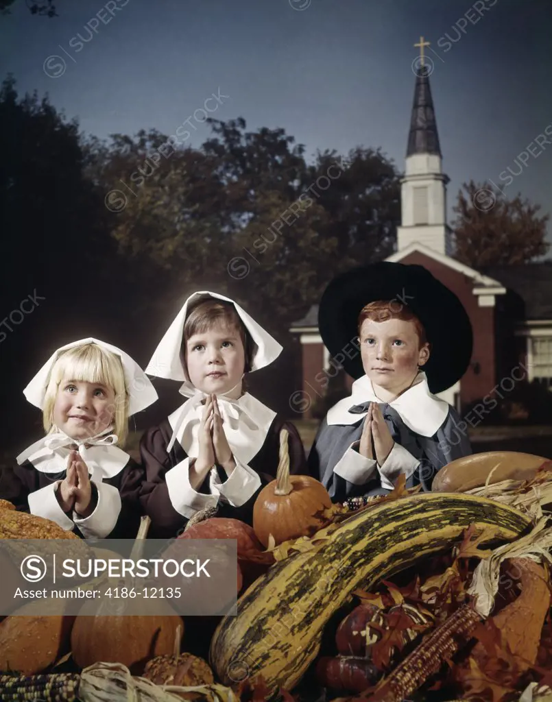 1960S Three Children Wearing Pilgrim Costumes Saying Grace Backdrop Of Church Spire