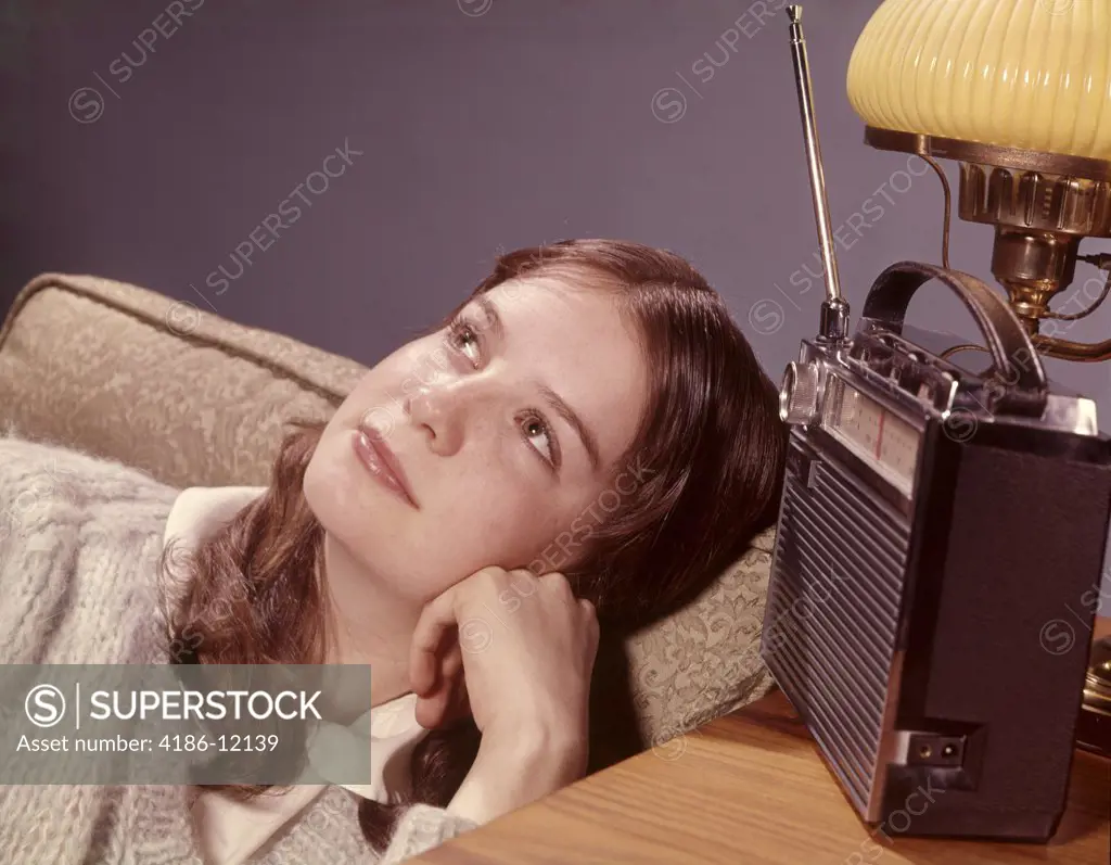 1960S Teenage Girl In Living Room Chair Listening To Portable Radio With Daydream Pensive Expression