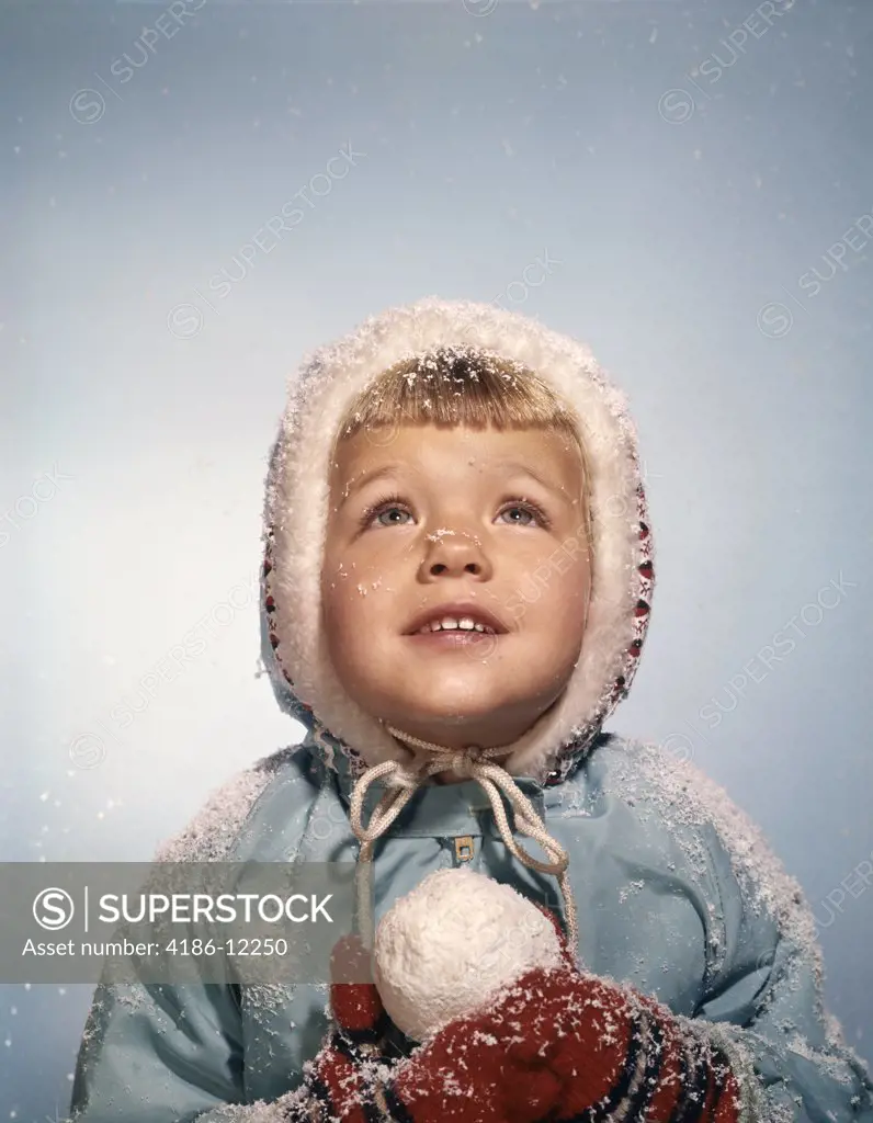 1960S Little Girl Holding Snow Ball Looking Up At Sky Hopefully Red Mittens White Knit Hat Blue Coat