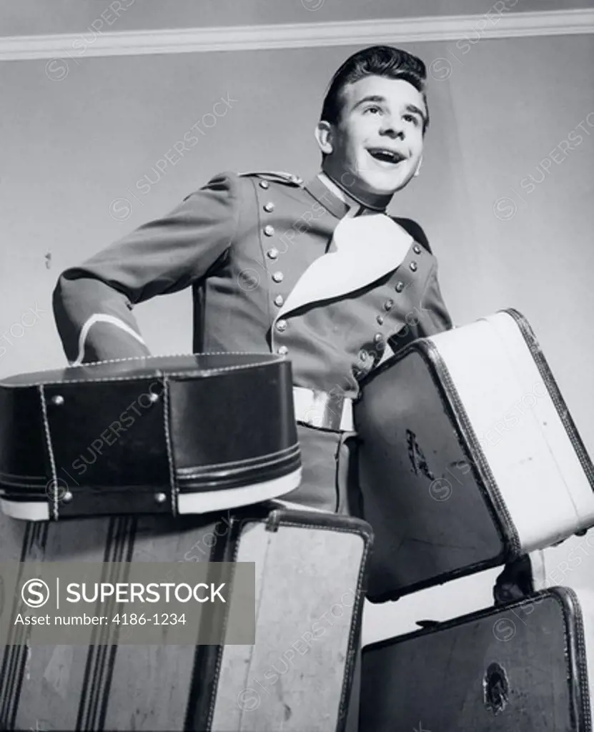 1950S Smiling Bellboy Carrying Four Bags Of Luggage