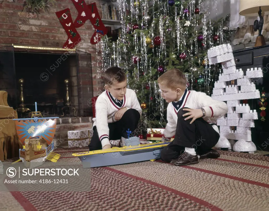 1960S Two Brothers Playing With Toy Model Aircraft Carrier And Lego Blocks By Decorated Christmas Tree