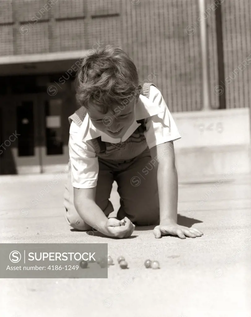 1950S Smiling Boy Ready To Shoot Kneeling On School Yard Ground Playing Game Of Marbles